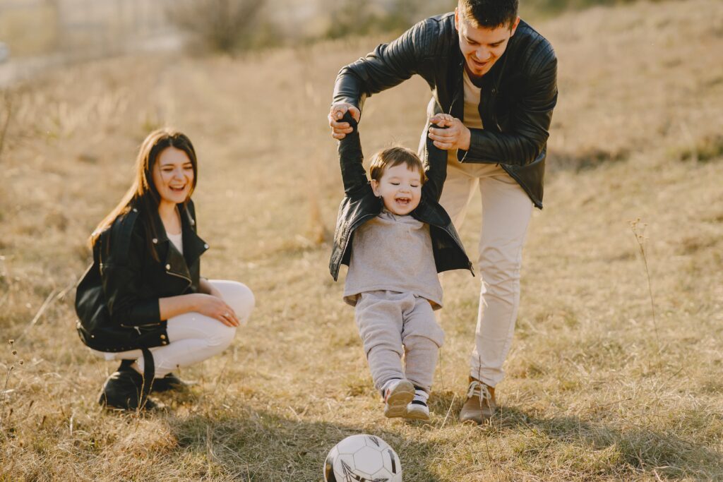 A father helping his child kick a soccer ball