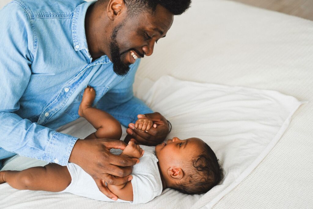 A father in a blue shirt laughing and playing with his baby