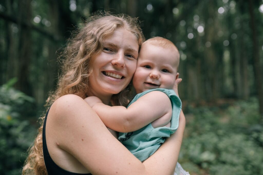 A mother smiling while holding her baby among trees